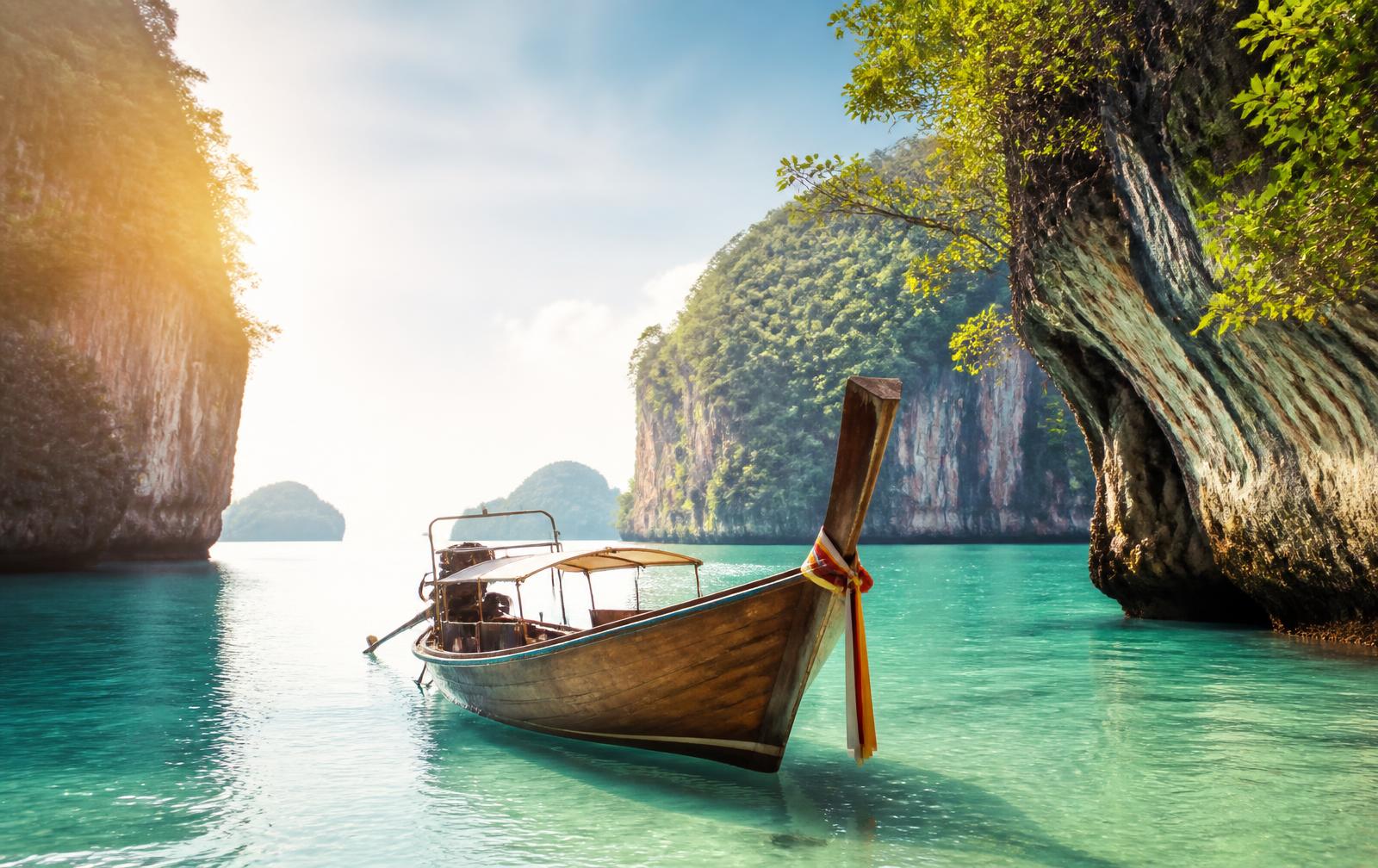 Longtail boat on calm turquoise water near Phuket's limestone cliffs