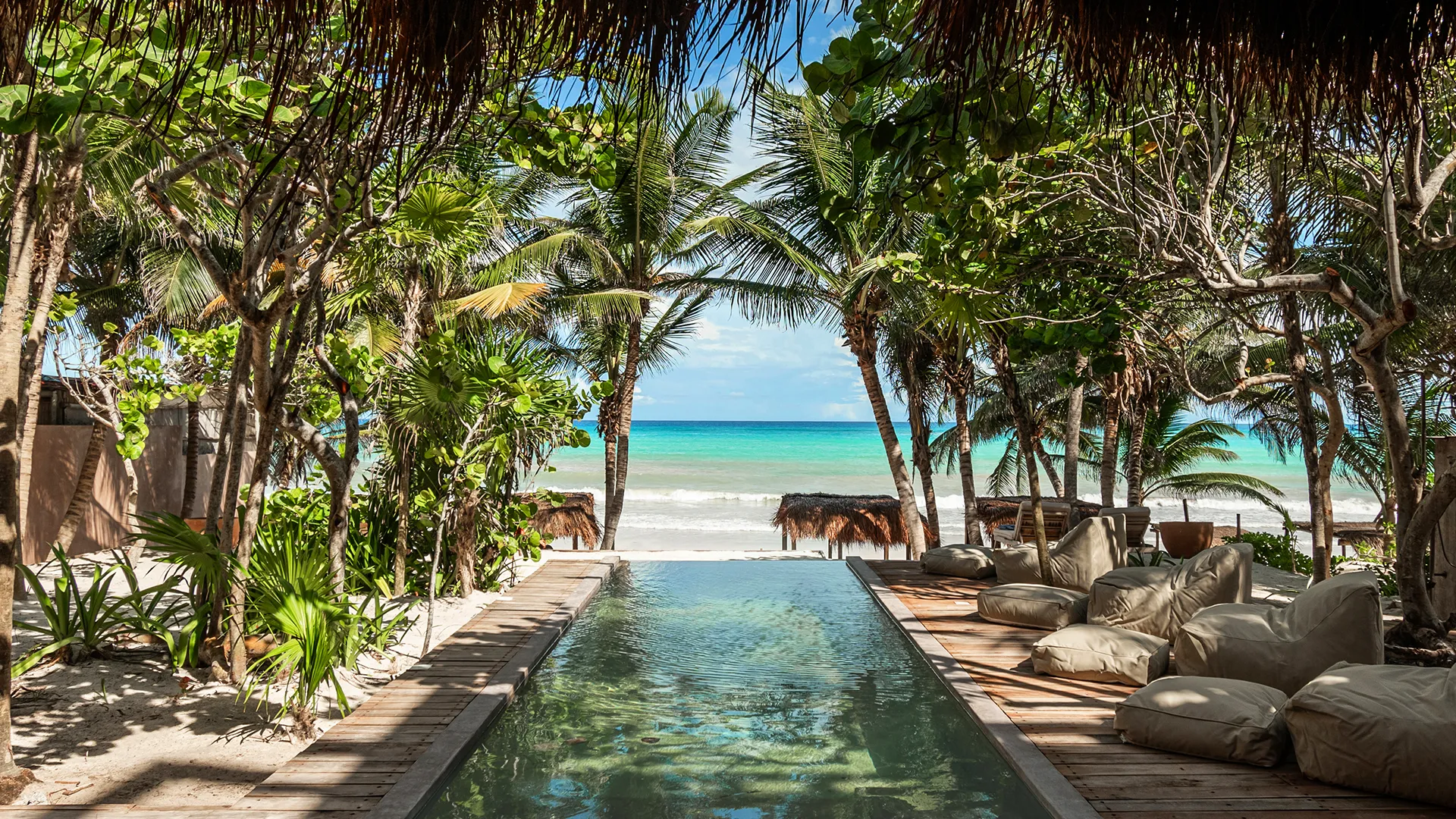Palm-lined pool looking out over the Caribbean beach in Tulum